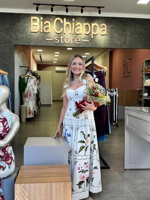 Bia segurando um buquê de flores em frente ao letreiro dourado da nova loja